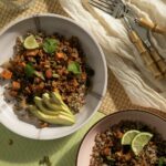 Two burrito bowls of sweet potatoes and grains sit in white bowls on a green background.