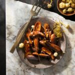 A bowl full of sticky eggplant with pickled garlic blossoms on top.