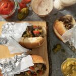 Three Italian Beef Sandwiches lay in various directions surrounded by fried peppers.