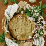 A homemade gluten-free blueberry pie surrounded by flowers. On the crust is a picture of a house.