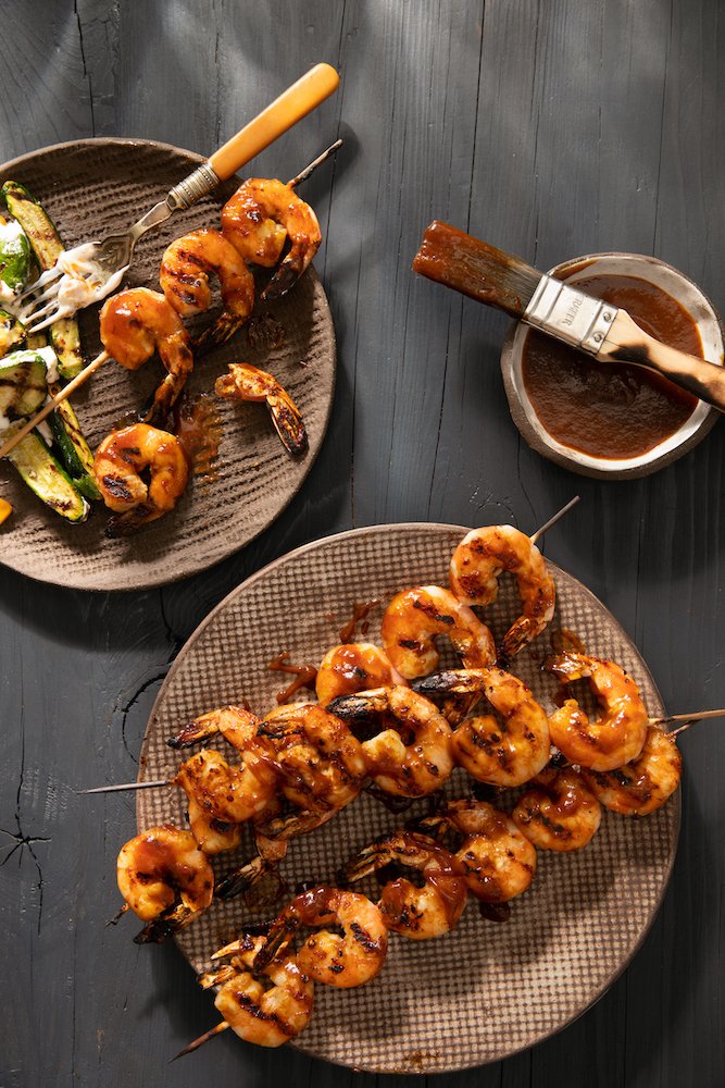 Apple Butter BBQ Sauce in a small bowl with a brush placed on it. Shrimp on sticks with bbq sauce on them.