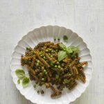 Green Pea Pasta with Sunflower Seed Pesto served in a while ceramic plate on a whitish rough surface