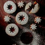 Pumpkin Pie Spice Linzer Cookies spread on a wooden surface, dusted with powdered sugar