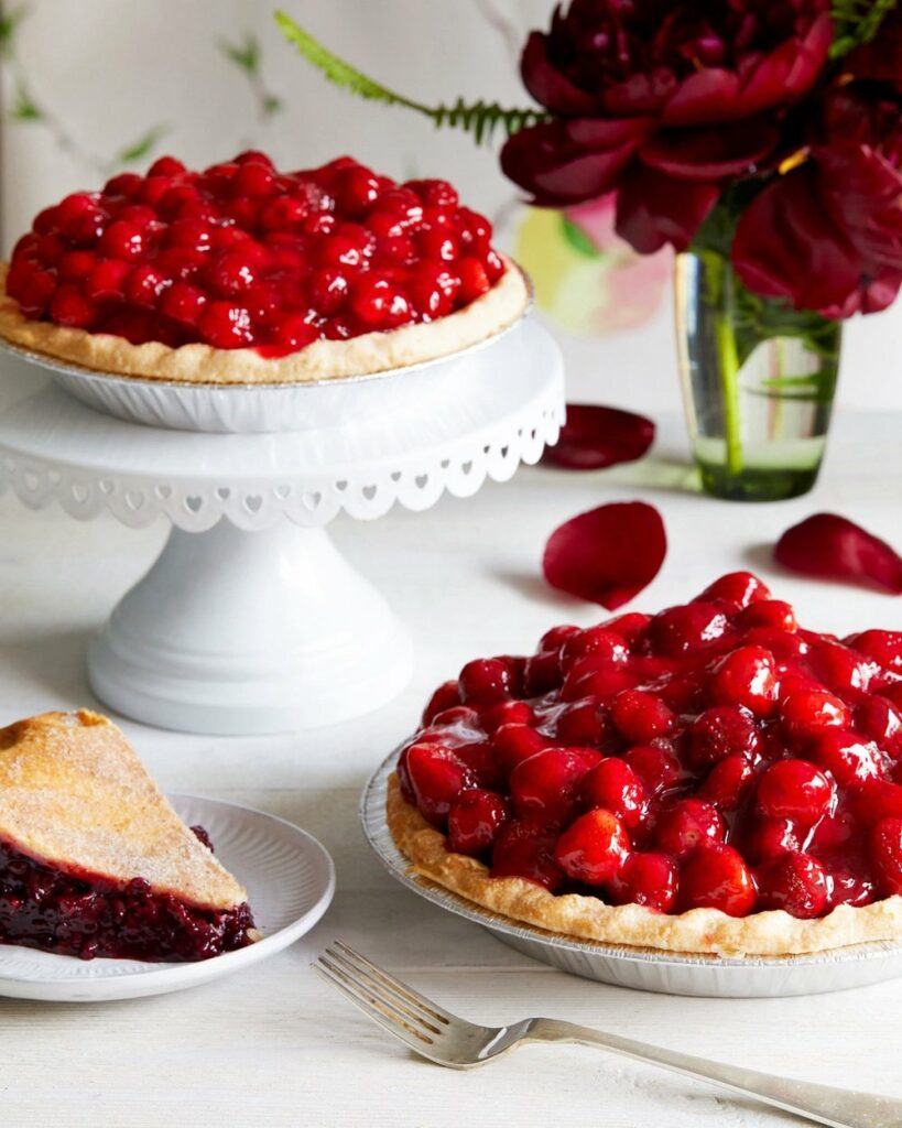 Raspberry Glaze Pie on two different plates along with flowers in a glass of water and a sandwich in a small plate