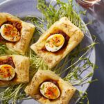 An aerial view of four Egg Masala Puffs on a grey plate with micro greens underneath.