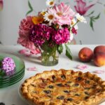 Gingered Peach and Blackberry Pie served in a glass plate with different-colored flowers in a glass on the side