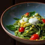 A spinach pasta dish with corn and tomatoes in a blue pasta dish