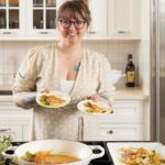 A mom holds two bowls of Rainbow Carrot Tortellini in a white kitchen.