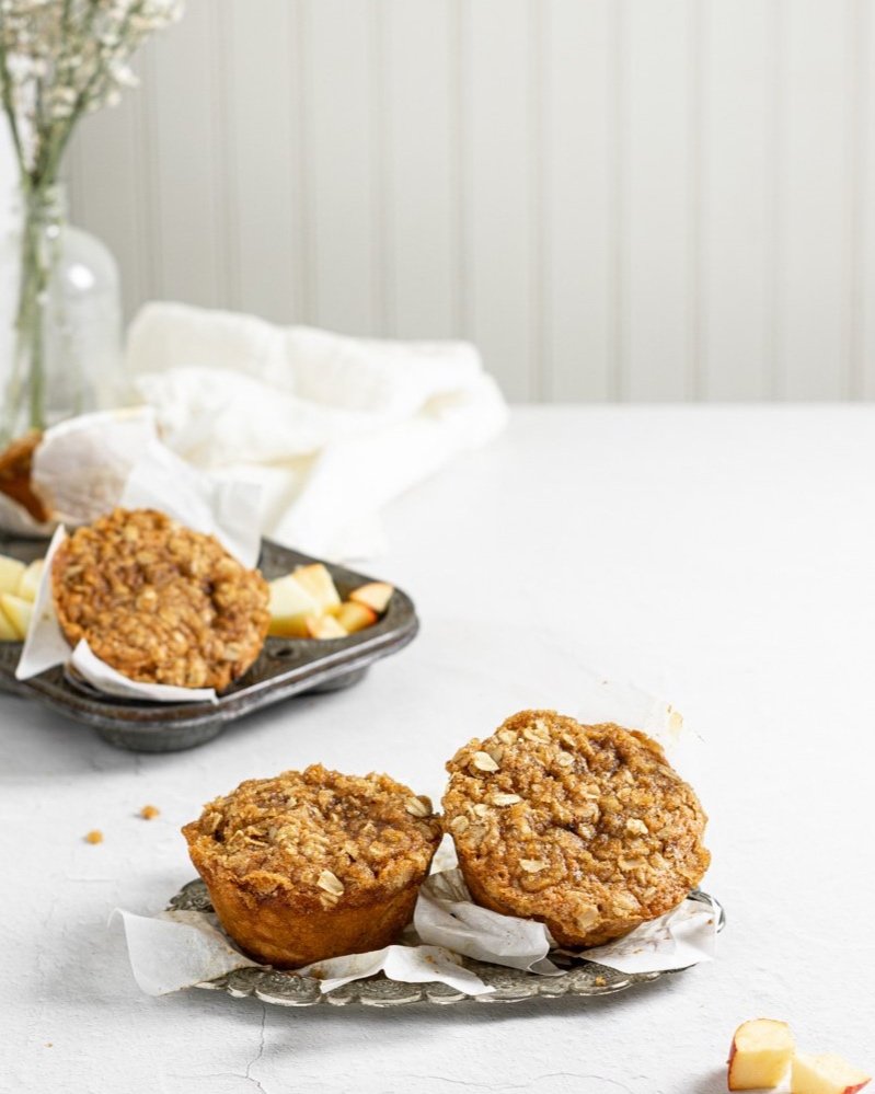 Two Vegan Apple Cider Muffins served on a small steel tray with small pieces of apple on a side