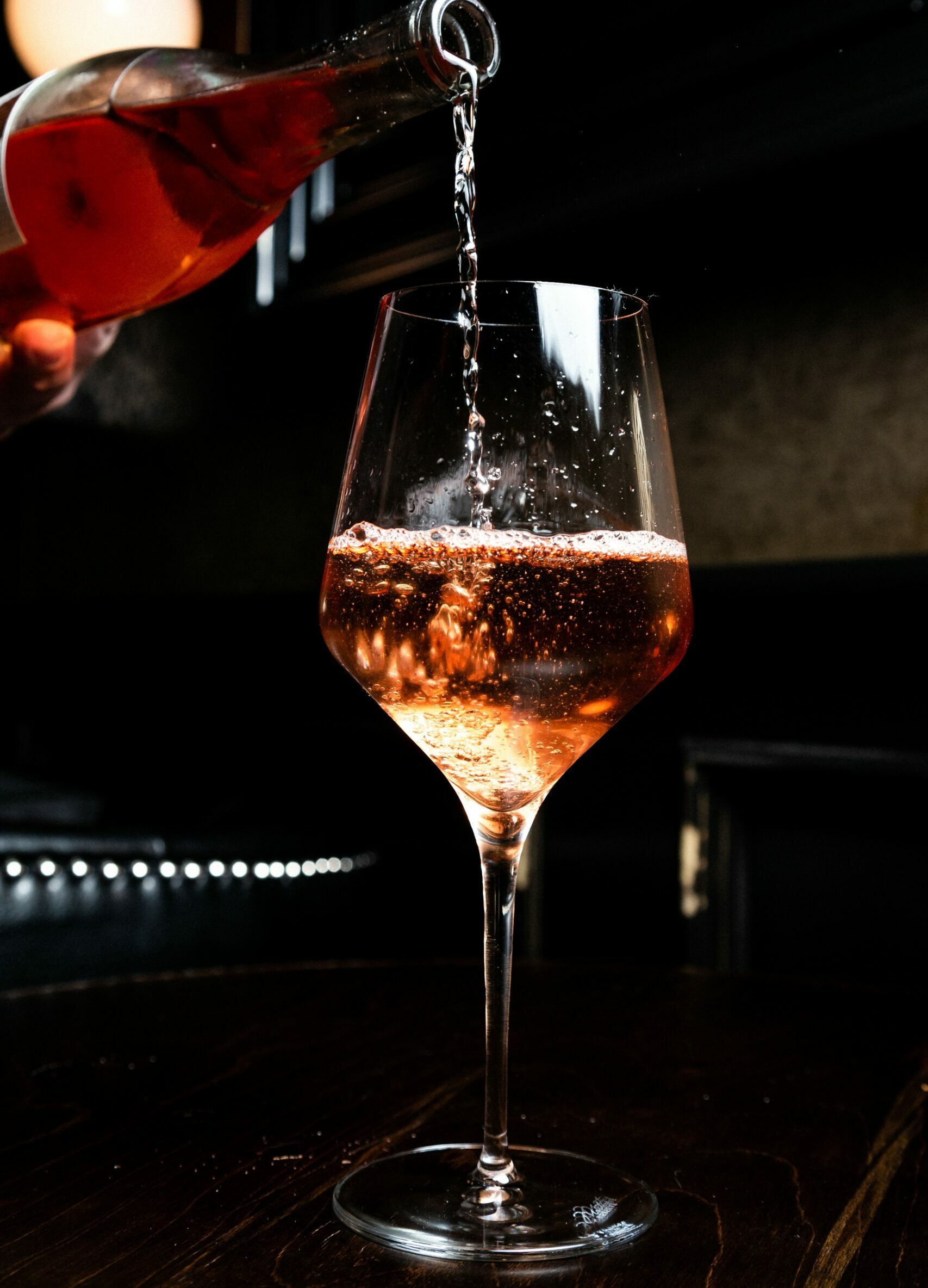 A hand in the top left of the frame pours a glass of pink rosé wine into a big wine glass. The glass is about halfway full. National rosé Day