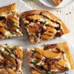 Four slices of Peach and Ricotta Pizza sit on a wooden background. They are orange and white in color and drizzled with a brown glaze.