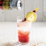 a clear glass with a white background with a pink Mexican Michelada cocktail being topped off with a can of hard seltzer