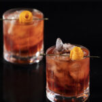 Two Negronis sit in rocks glasses garnished with orange peel. Classic Negroni Recipe