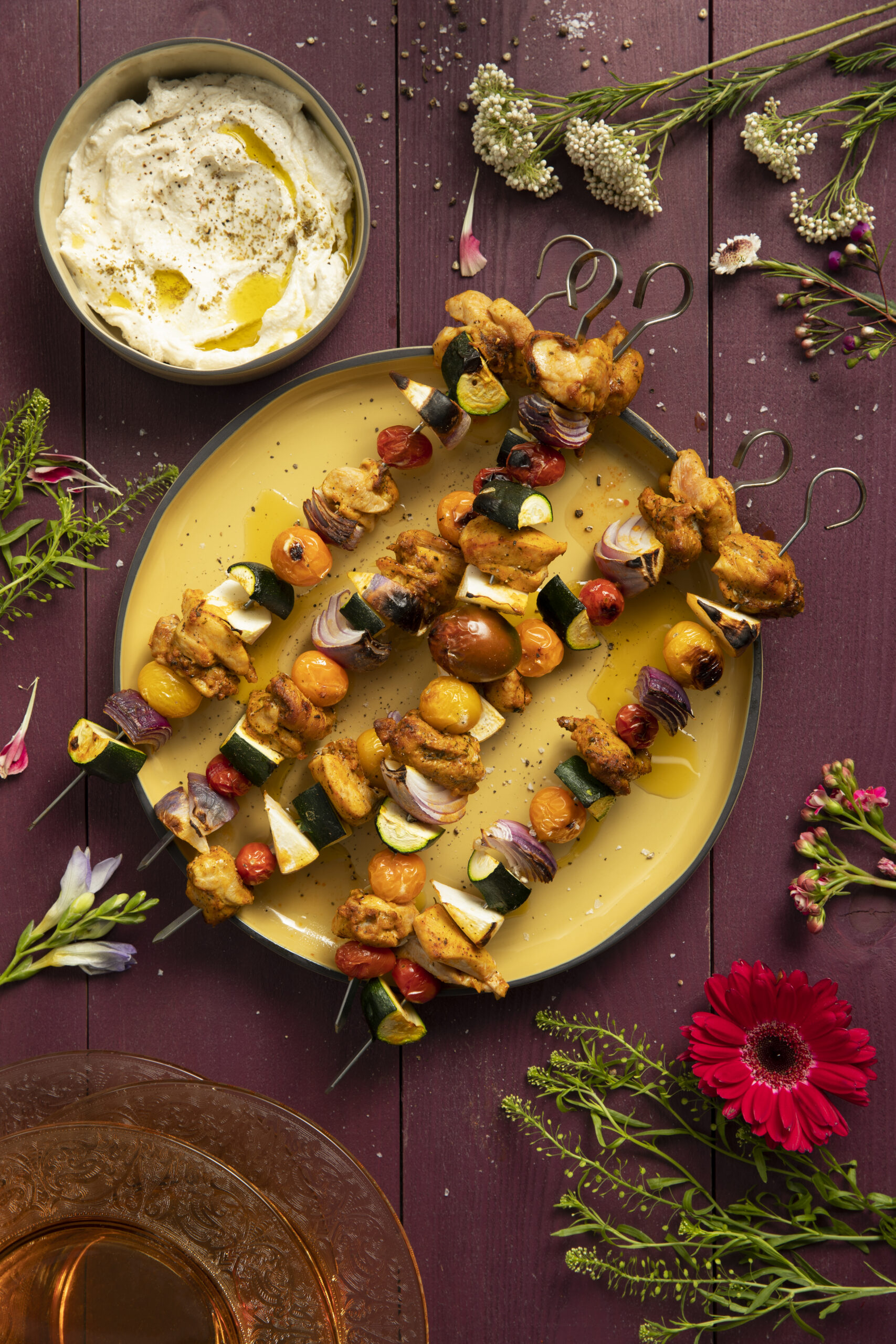 An aerial view of Shawarma Chicken Kabobs on a yellow plat surrounded by flowers. kabob recipe