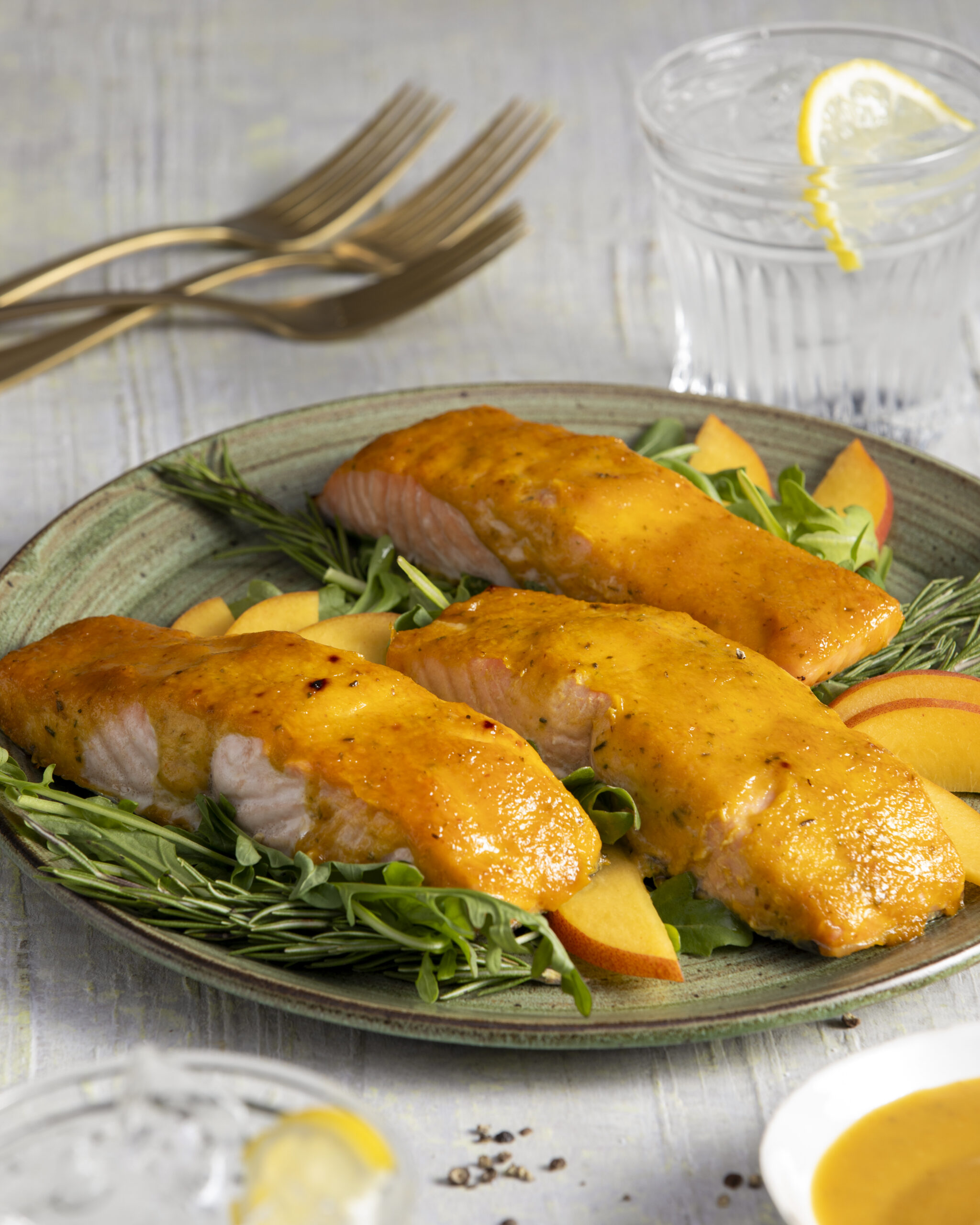 Three portions of salmon with a peach and yellow tomato sauce on a green plate with a white background.