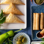 A flat-lay image of spinach pies and spring roll appetizers .