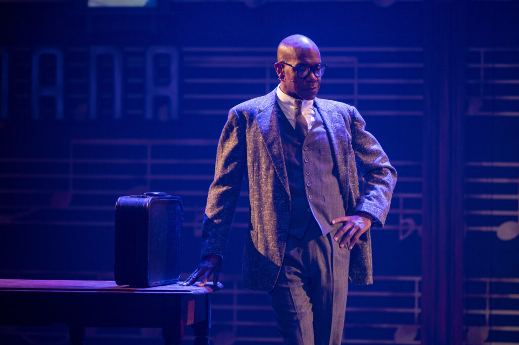 A black man in a suit leans on a table with a briefcase in Billy Strayhorn: Something to Live For