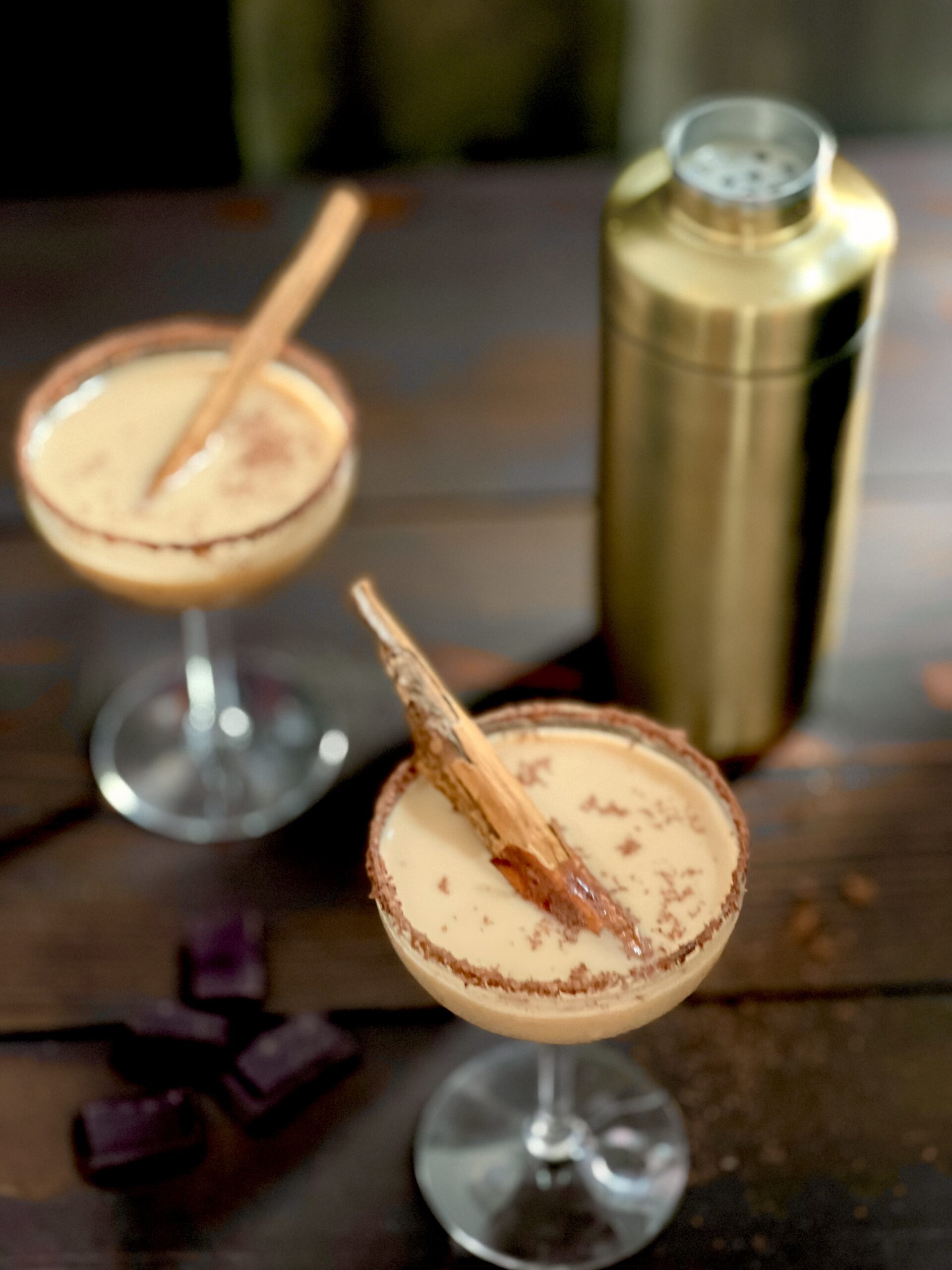 an overhead shot of two cocktails in martini glasses. down in color, with shaved chocolate on the rim, the pumpkin spice cocktails are garnished with a cinnamon stick