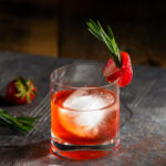 A cocktail orange in color sits in a rocks glass, garnished by a strawberry. Punch Drunk Negroni Cocktail Recipe