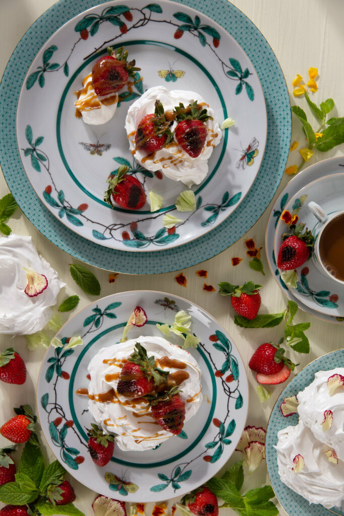 A beautifully presented Pavlova with Roasted Strawberries and Coconut Jam, served on an exquisite plate, showcasing the art of porcelain and stoneware craftsmanship.