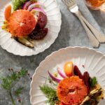 A pickled vegetable salad plated on white plates with silverwear.