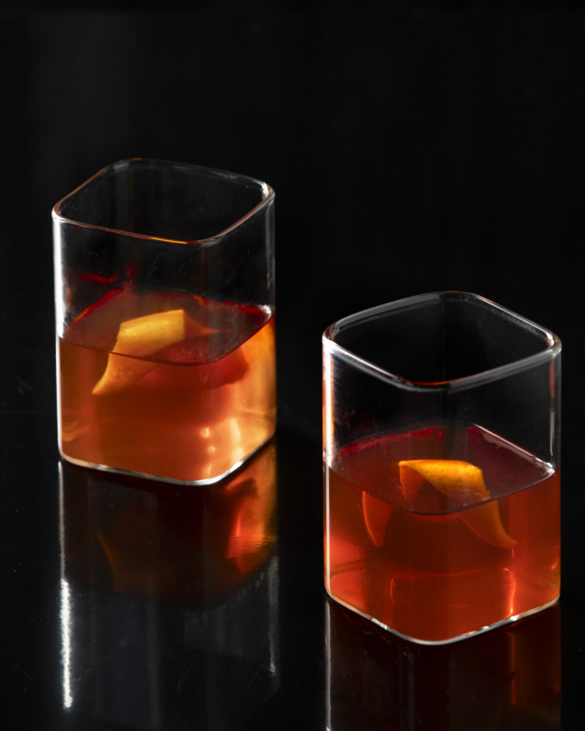 Two cocktails brown in color in square rocks glasses