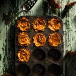 Flat-lay image of a muffin tin filled with sweet potato rosettes on a weathered table.