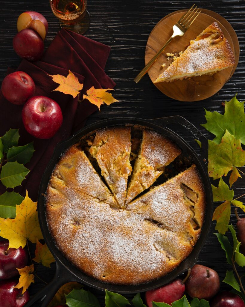 An aerial shot of a Stone Fruit Polenta Cake with a few slices precut and leaves and apples surrounding the cake. Stone Fruit Polenta Cake Recipe