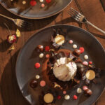 An aerial view of a peppermint dessert on a grey plate drizzled in chocolate and decorated with red and white candy