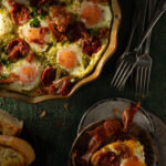 An easy breakfast bake made with eggs, presented in a pie dish in the upper left corner, with a piece on a plate, and forks to the right of the pie dish.