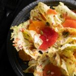 A close up picture of bitter green leaves littered with sliced fruit in the bitter greens salad.