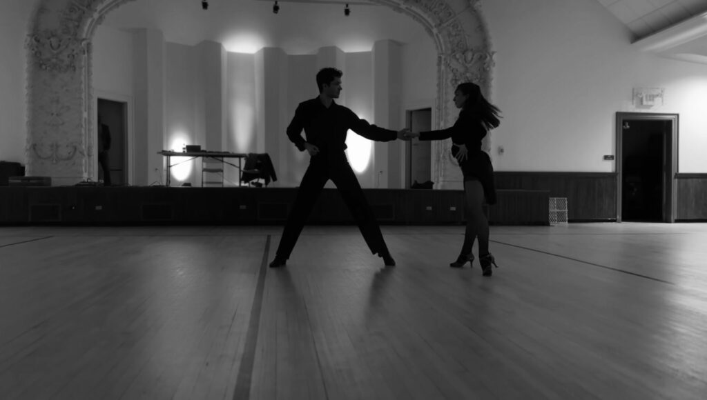 Two people dance silhouetted in black and white across a dance floor.