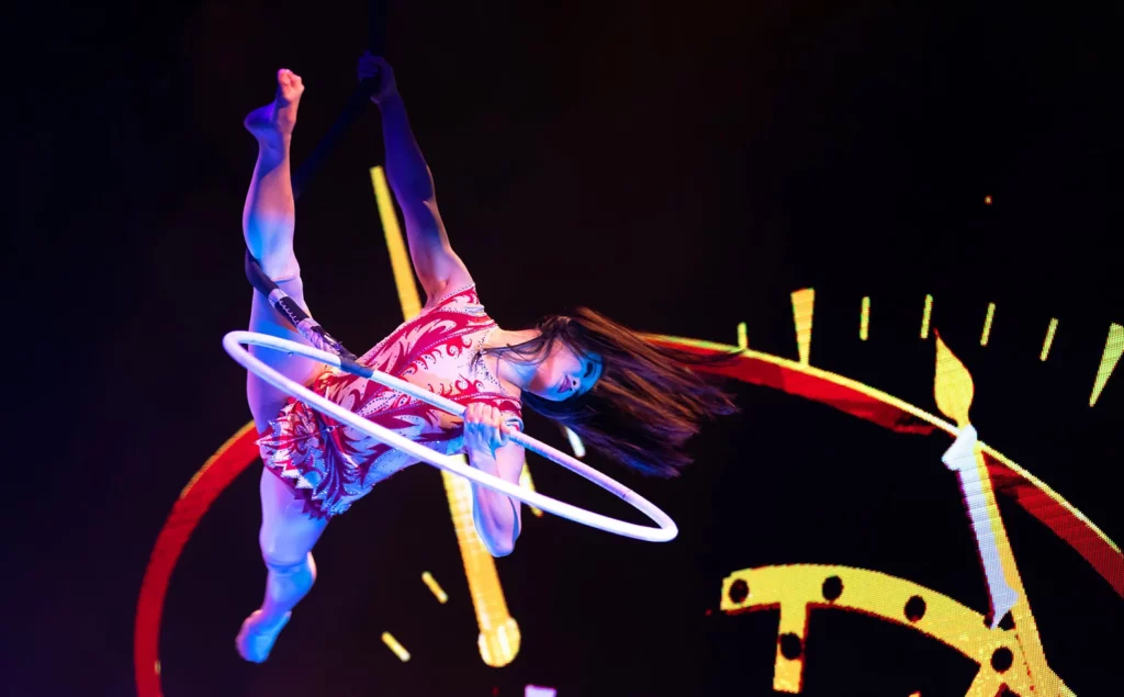 An acrobat spins on a hoop in the sky in a patterned leotard.
