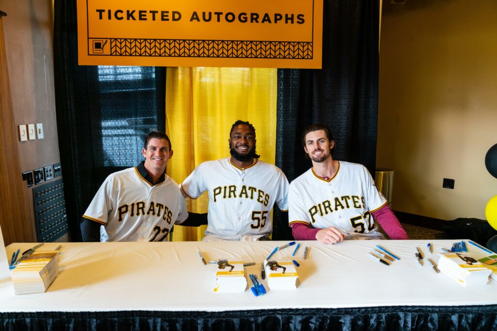 Three pirates players sit at an autograph table in Pittsburgh in their jerseys.