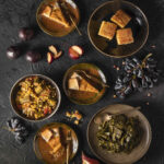 A variety of plates filled with different sides of cornbread, collard greens, and so much more is laid out on a big black table.