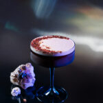 A espresso martini cocktail for Sagittarius sits in a glass, topped with espresso powder with a crystal gem to the left.