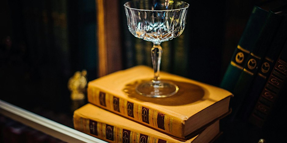 a cocktail glass on top of a stack of yellow books on a book shelf.
