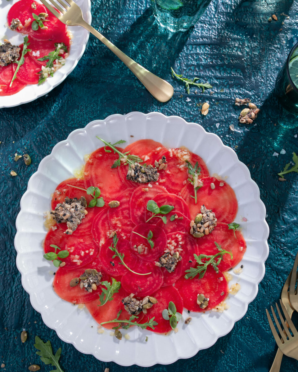 A white plate holds an array of thinly sliced beats with an herbal topping to make a Beet Carpaccio with a Citrus Vinaigrette.