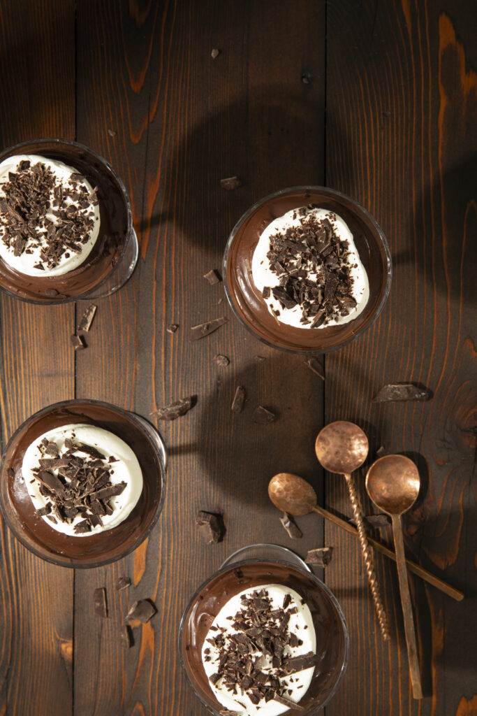 Chocolate Cremeux - pudding served in four glasses with chocolate chunks spread across the wooden table alongside three spoons