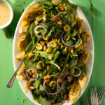 Baby Kale Salad with Citrus-Marinated Artichoke Hearts and Lemon Vinaigrette on a white plate with a fork in the salad and a container of dressing to the left.