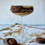 An Adventurefuls® Cocktail is placed in a cocktail glass drizzled with chocolate syrup and rim coated in crushed Adventurefuls® cookies. Three Adventurefuls® cookies sit in front of the glass.