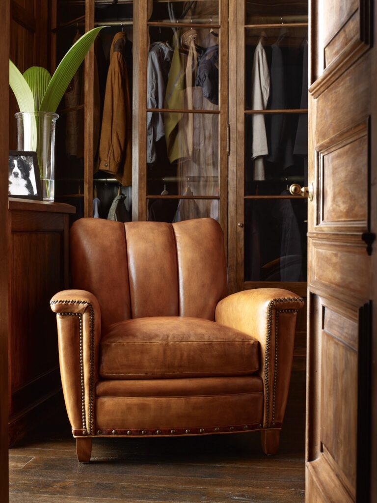 A brown leather chair from Sewickley business Antiquarian sits in a living room set up with light shining in from the left side.