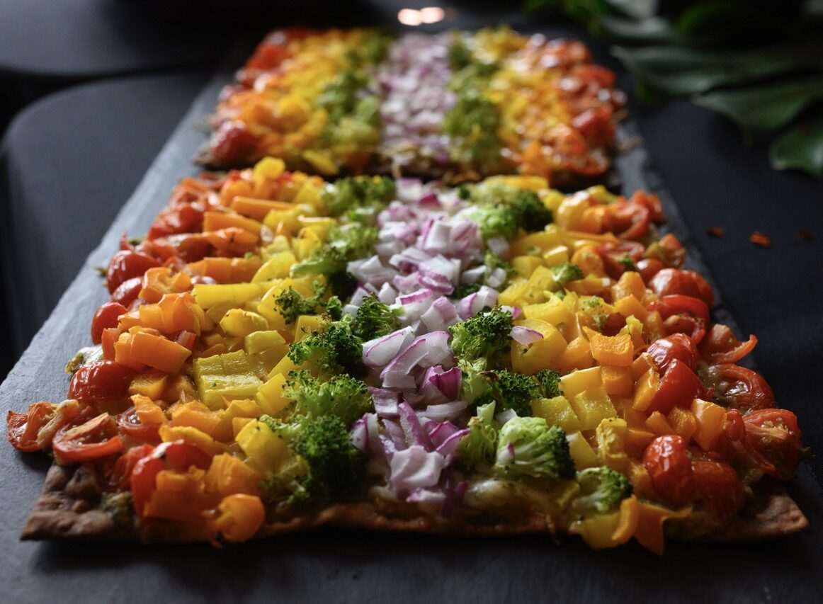 Two flatbread pizzas topped with a rainbow of chopped veggies sitting on a black tabletop.