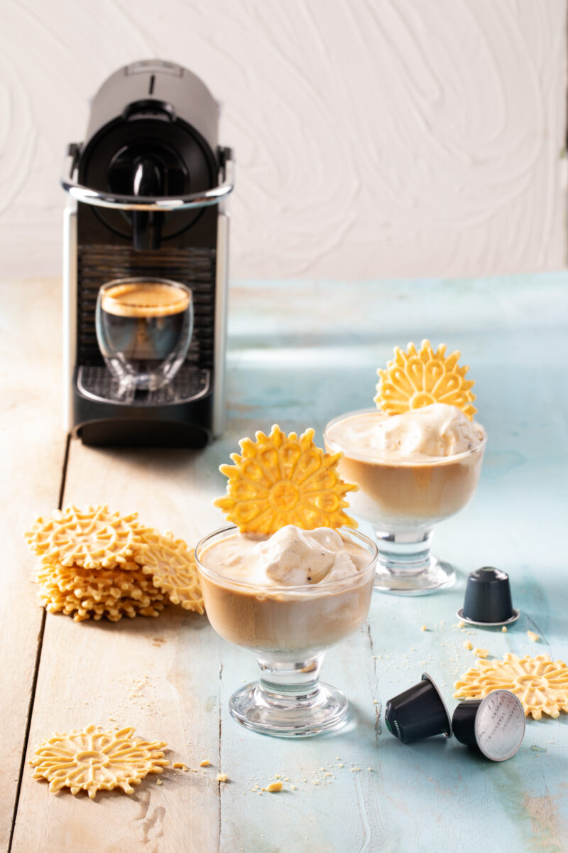 Two glasses of Nespresso Affogato with pizzelle garnishes in front of a Nespresso machine with a shot of espresso brewed beneath it.