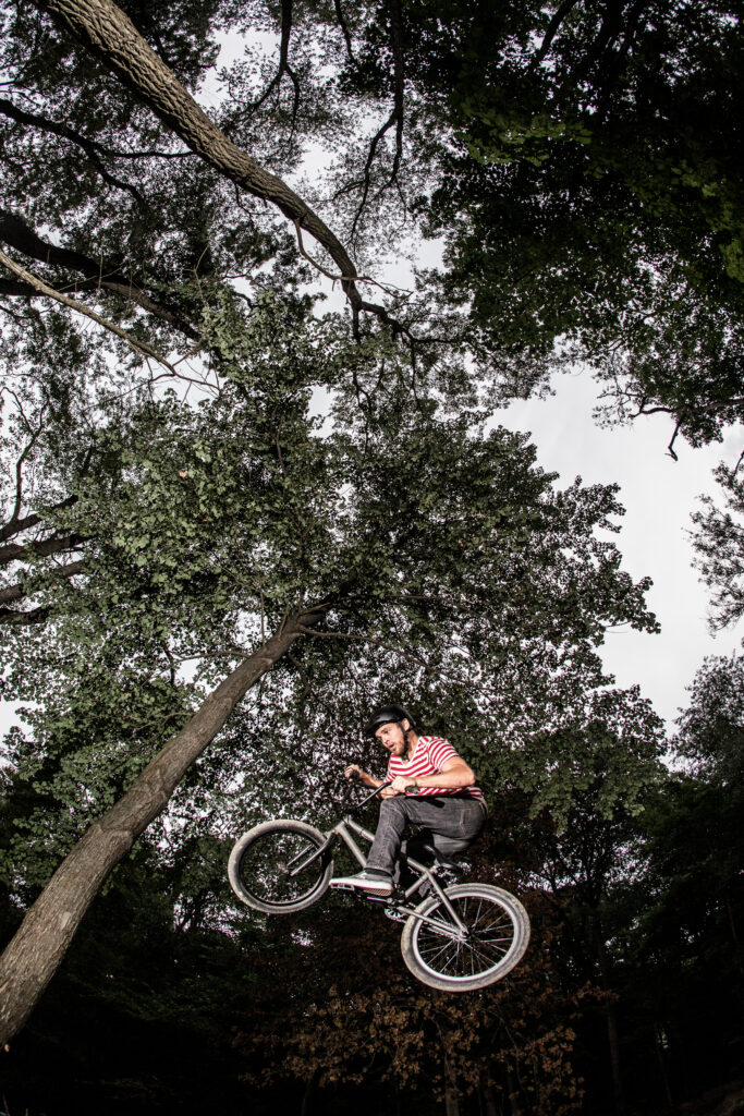 A guy riding a BMX bike caught mid-air during a stunt in a forest backdrop