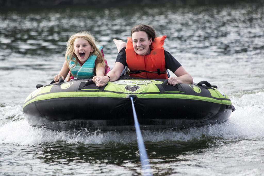A little girl and a grown up female doing water tubing on a green and black tube 