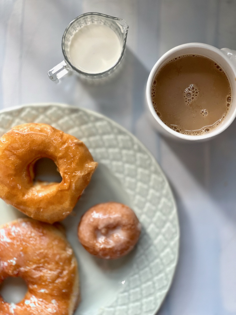 A plain glaze donut on a white background with a cup of coffee