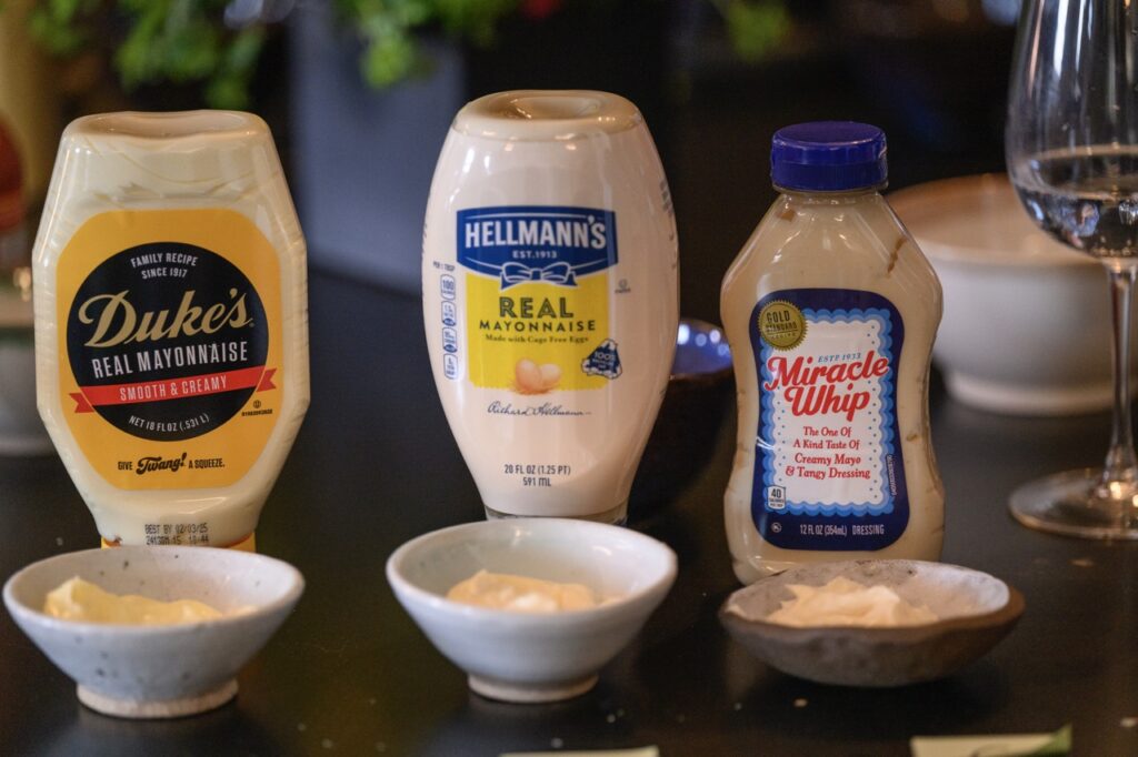 Three bottles of mayo sit behind three small white bowls of mayo.