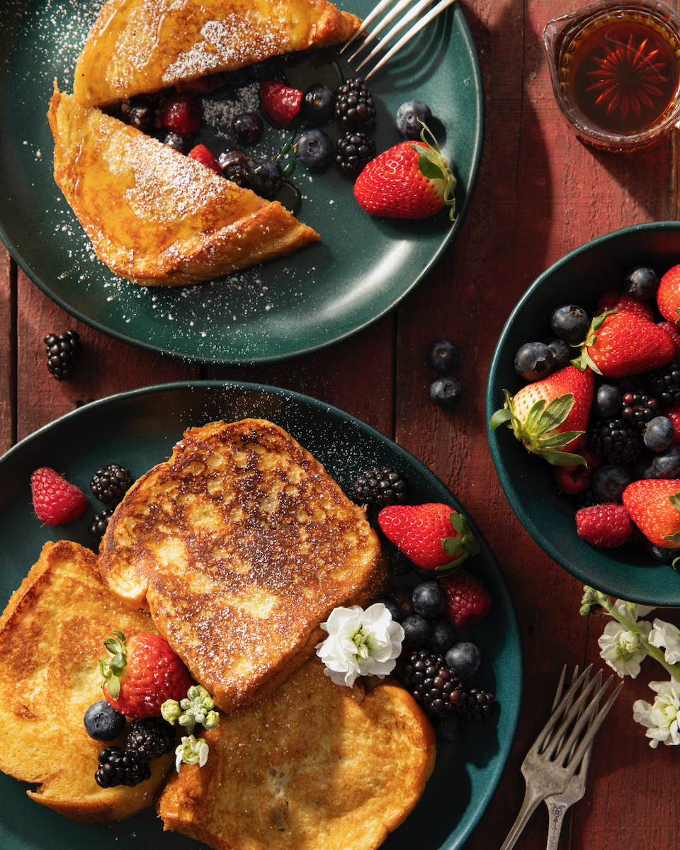 A plate of French toast with berries on a green plate.