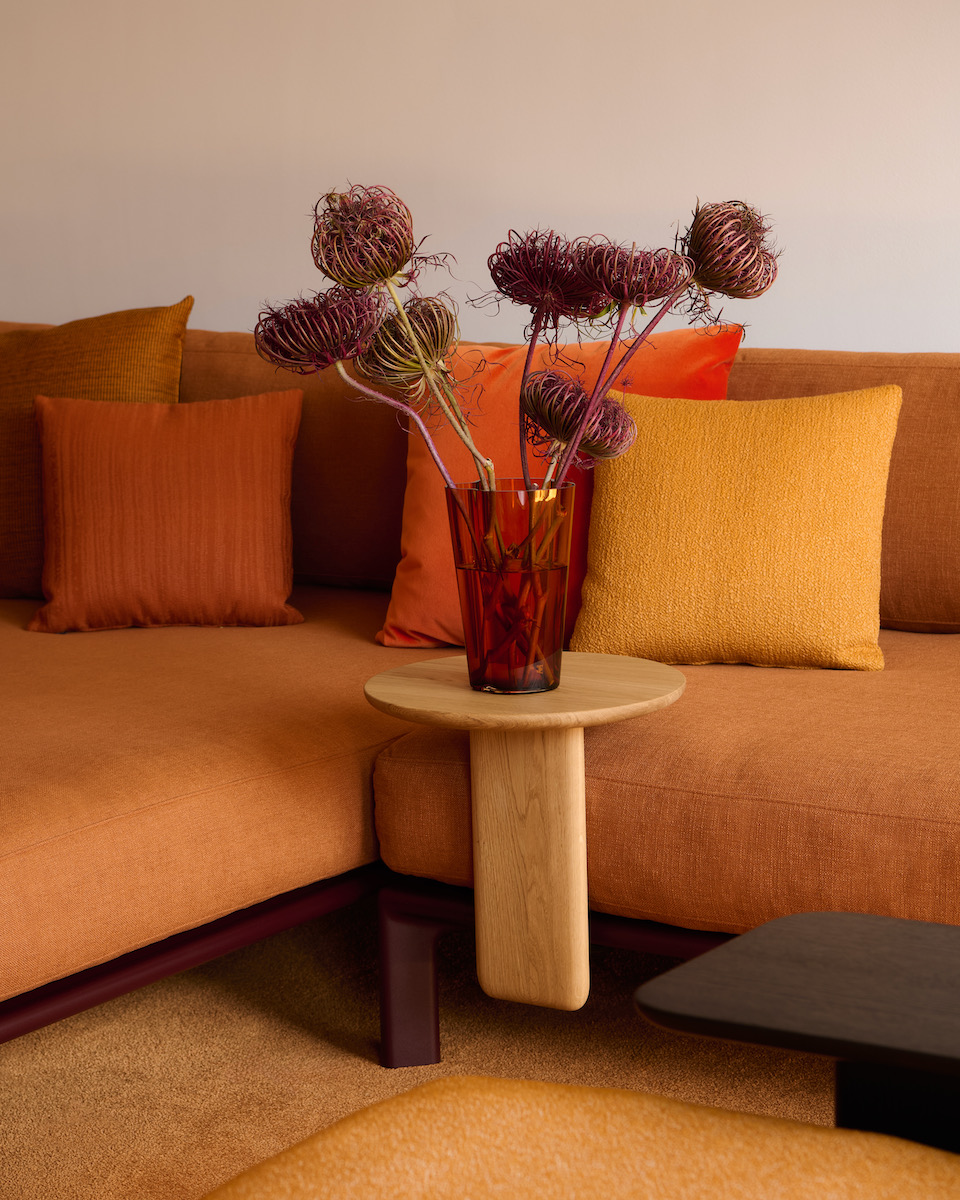 An orange sofa with two cushions and a side table with a flower arrangement on it